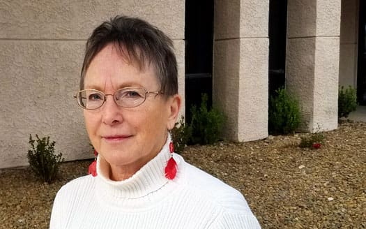 Woman in white sweater with red earrings.