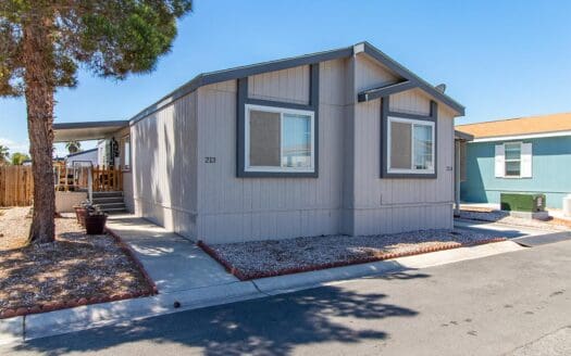 A grey single-wide mobile home with a tree.